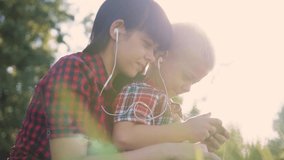 happy family funny video slow motion play music teamwork outdoors. Mom and son listen to music on smartphone in the same headphones for two. happy family mother woman lifestyle and son little boy