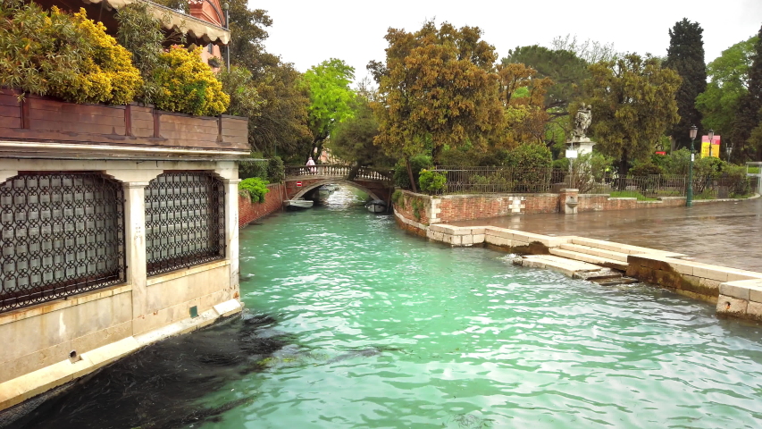 VENICE, Italy - May 2019: Romantic landscape in rainy weather. A channel with blue clear water, in the distance a bridge over which unidentified people pass. Slow motion.