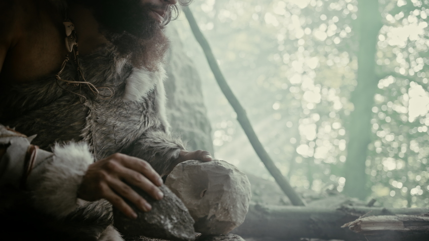 Primeval Caveman Wearing Animal Skin Hits Rock with Sharp Stone and Makes Primitive Tool for Hunting Animal Prey. Neanderthal Using Hand axe to Create first Wheel. Slow Motion Shot Royalty-Free Stock Footage #1037017259
