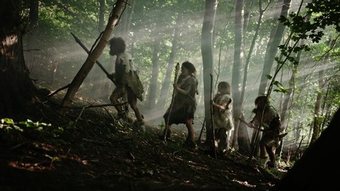 Tribe of Hunter-Gatherers Wearing Animal Skin Holding Stone Tipped Tools, Explore Prehistoric Forest in a Hunt for Animal Prey. Neanderthal Family Hunting in the Jungle or Migrating. Side View