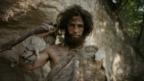 Portrait of Primeval Caveman Wearing Animal Skin Holding Stone Tipped Hammer. Prehistoric Neanderthal Hunter Posing with Primitive Hunting in the Jungle. Looking at Camera Stockvideó
