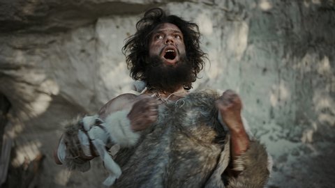 Portrait of Primeval Caveman Wearing Animal Skin Does Threatening Chest Beating and Screaming, Defending His Cave and Territory in the Prehistoric Times. Prehistoric Neanderthal or Homo Sapiens Leader