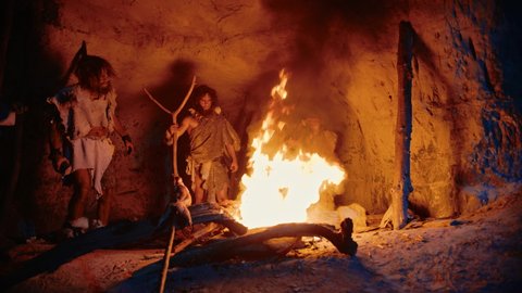 Tribe of Prehistoric Hunter-Gatherers Wearing Animal Skins Stand Around Bonfire Outside of Cave at Night. Portrait of Neanderthal / Homo Sapiens Family Doing Pagan Religion Ritual Near Fire