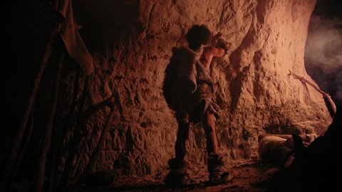 Primitive Prehistoric Neanderthal Wearing Animal Skin Draws Animals and Abstracts on the Walls at Night. Creating First Cave Art with Petroglyphs, Rock Paintings Illuminated by Fire. 8K UHD.
