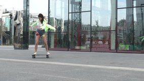 A beautiful girl from Russia is riding a skateboard along the street. Modern girl in motion. She is wearing a bright jacket with a light green hood.