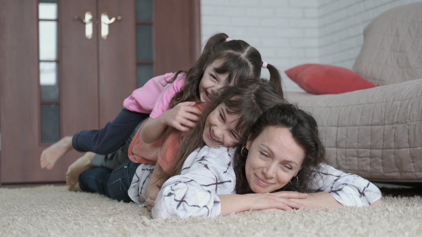 Children have fun with mom. Cheerful daughters lay down on mother.