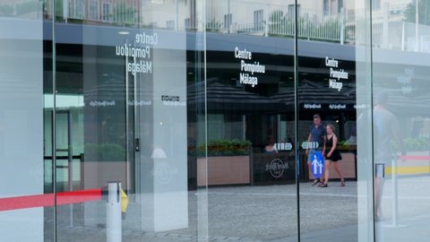 Malaga/Spain - 09-04-2019 : Sliding transparent entrance doors of the modern art museum named Pompidou in Malaga Spain. Reflections of the surrounding buildings and tourists in the glass window