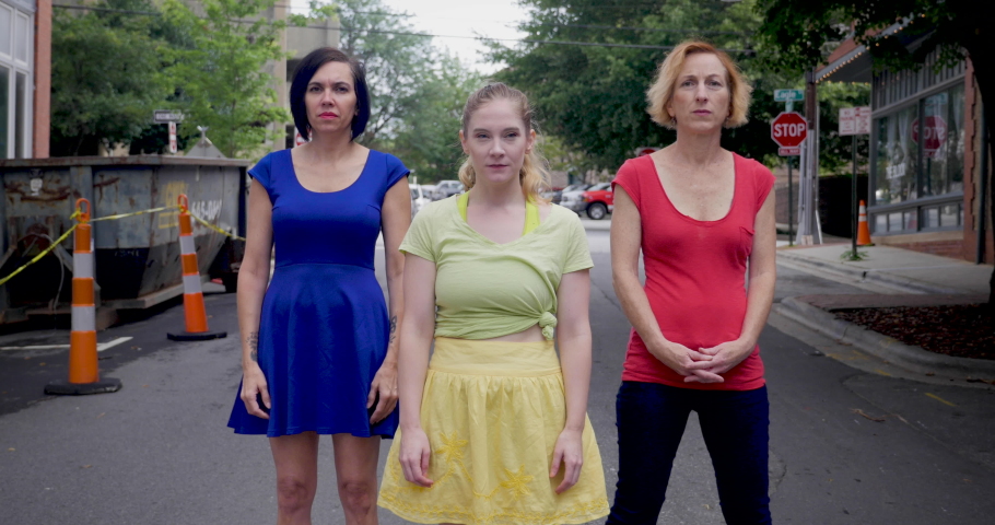 Three women wearing primary colors dancing in the middle of an urban street in the city