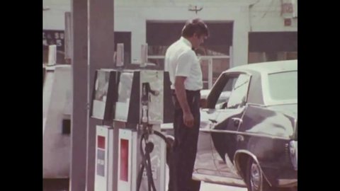 CIRCA 1970 -- A gas station attendant fills a customer's tank, and looks under the hood at a full service station.