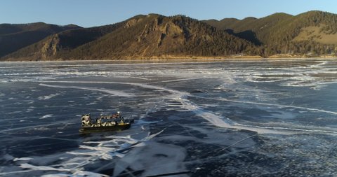 Hovercraft moving on frozen Lake Baikal by mountains during sunny day