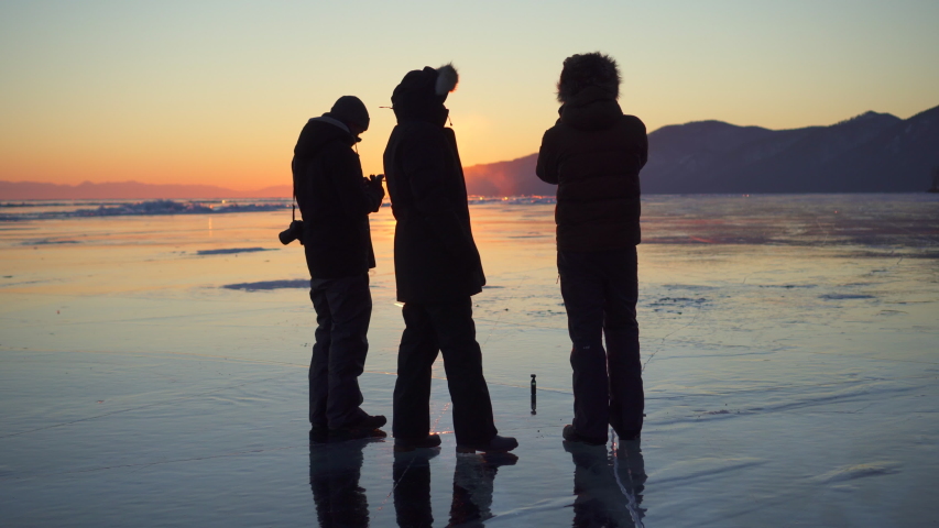 Male tourist talking while standing on frozen Lake Baikal against orange sky during sunset