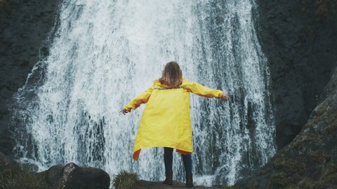 Young woman arms outstretched behind spectacular waterfall in Iceland. Shot of young woman outstretching arms by majestic waterfall. Success and achievement concept.