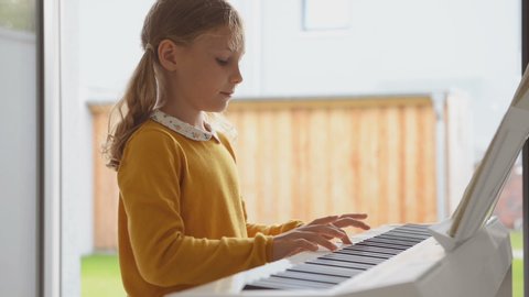 Portrait of pretty little girl having piano lesson at modern white e-piano at home