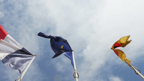 Panning in slow motion to the Flag of Germany, Flag of Europe and French Tricolor Flag against clear blue sky
