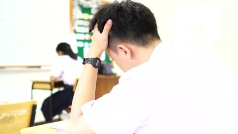 stressed headaches, Asian boy student studying for test or exams in classroom, learning lessons doing final exam at high school with Thailand uniform in class room. Education system concept.