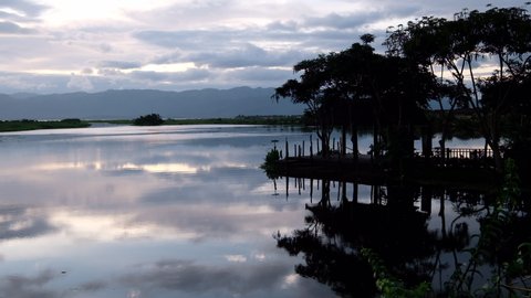 beautiful sunset reflection of Inle lake in Shan State Myanmar. Jetty and trees silhouette above peaceful lake