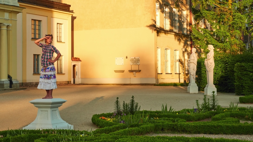 Little girl is pretending to be statue. Branicki Palace is a historical edifice in Bialystok, Podlaskie Voivodeship, Poland. The palace complex with gardens, fountains, pavilions, sculptures.
