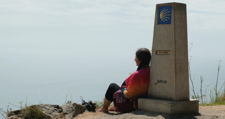 Woman doing pilgrimage to Fisterra, or Finisterre, after having completed the Santiago Walk. Person leaning on the marker KM 0 and contemplating the ocean.