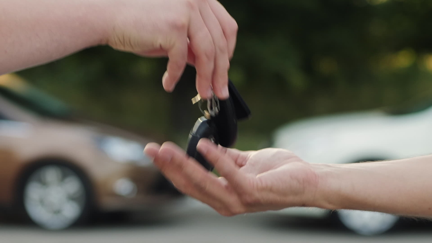 Man hands keys to another person, close-up of hands on a blurred background of cars