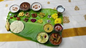 Video of traditional Indian lunch Onam sadhya, boiled rice served on green banana leaf with many spicy hot curries and lots of sweet dessert for Kerala harvest festival in India. Silk saree background