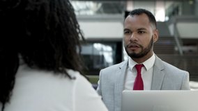 Thoughtful young businessman talking on smartphone. Focused African American man communicating with interlocutor while sitting at table with colleague. Business communication concept
