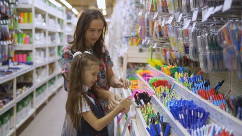 Mother and daughter in a stationery store choose school supplies. Family in supermarket chooses stationery writing pens.