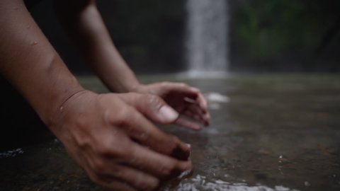 scene of man washing hands by the river near waterfall