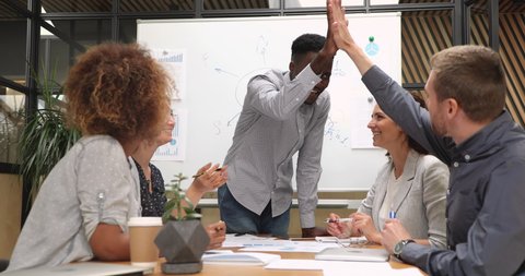 Happy diverse businessmen designers give high five during team corporate brainstorm, african group leader and caucasian partner coworker celebrate good successful teamwork result at company briefing