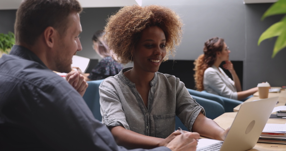 Female african american professional mentor manager consulting caucasian male client training intern helping colleague with corporate project software using laptop computer working together in office