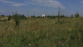 Video clip of summer landscape, field with grass and factory pipes in the background