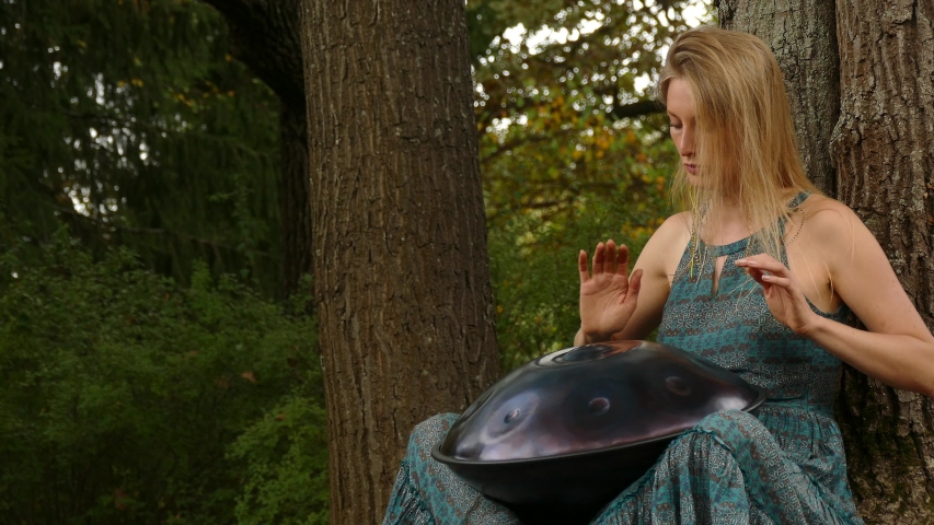 Beautiful young woman plays a hangpan in the autumn park