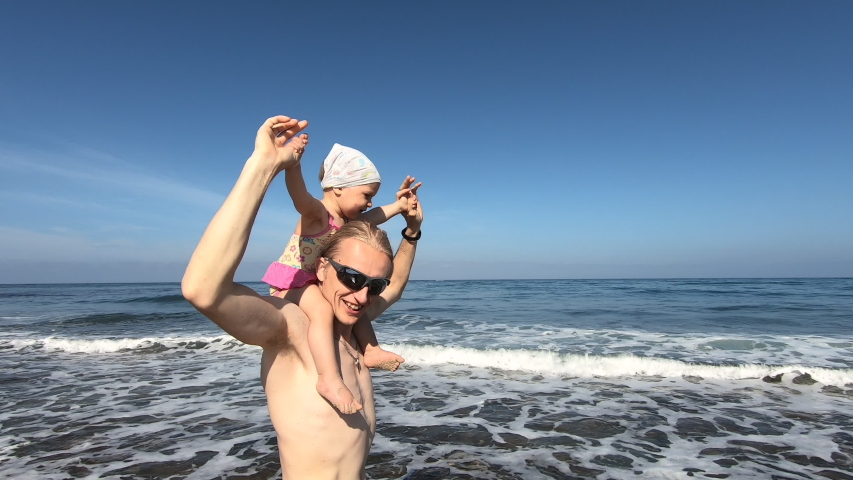 Little daughter sit on the father shoulder and enjoy beautiful sea view with big wave. Active family travel to Cyprus, Paphos and spending time together