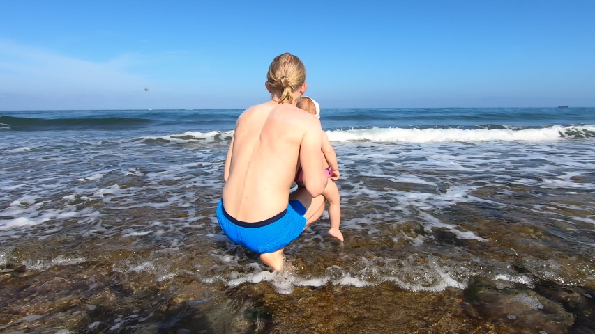 Young father hold his little daughter on the hand and show beautiful sea with big wave. Active family travel to Cyprus, Paphos and spending time together