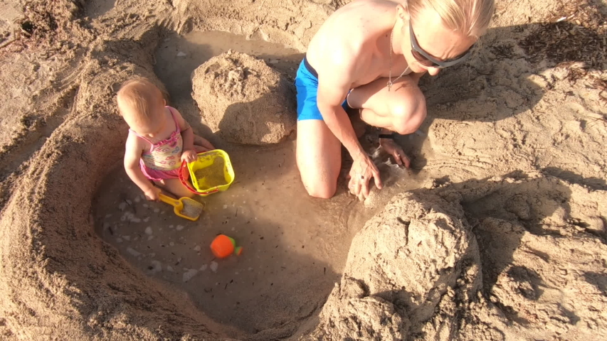 Father and daughter building sand castle on the beach at sunny day. Top view