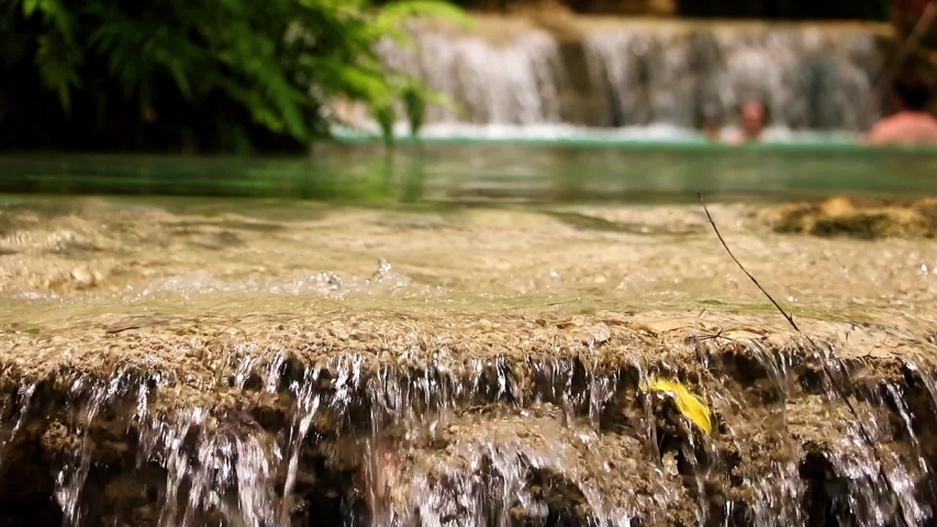 Water cascade in tropical jungle with swimming blurred people in lagoon on backround. The Kuang Si Falls, known as Tat Kuang Si Waterfalls Luangprabang, Laos.