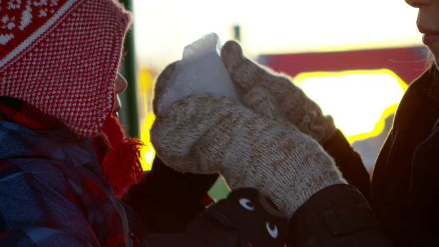 Young boy and mother playing with chunk of ice at park in winter - dont eat yellow snow
