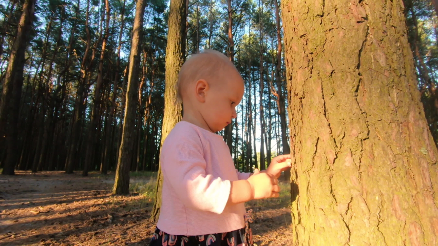 Little baby girl smiling and walking in the forest at sunset time