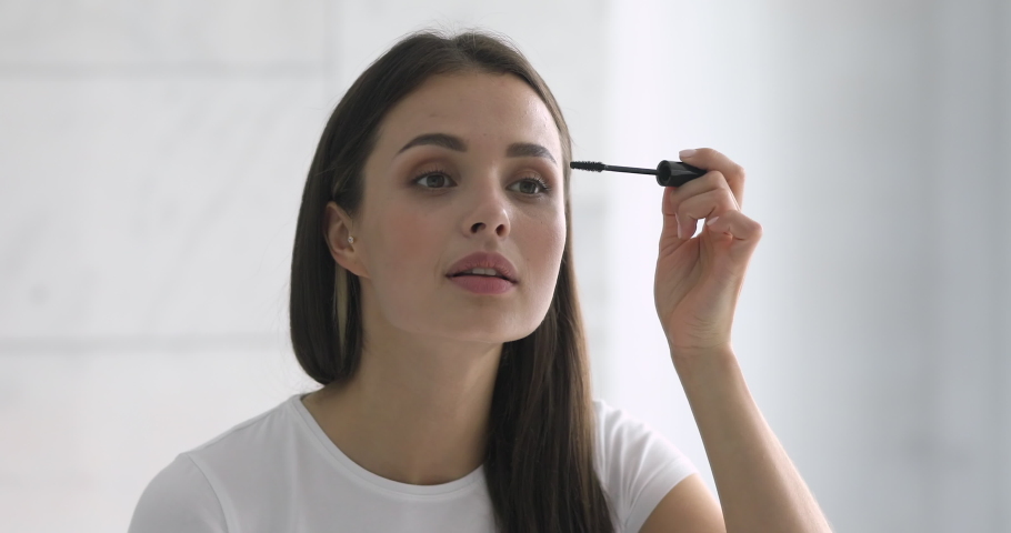 Confident happy young woman holding mascara apply on eyeleashes prepare getting ready in the morning, smiling beautiful girl doing make up put cosmetics on face looking in mirror in bathroom at home Royalty-Free Stock Footage #1037144993