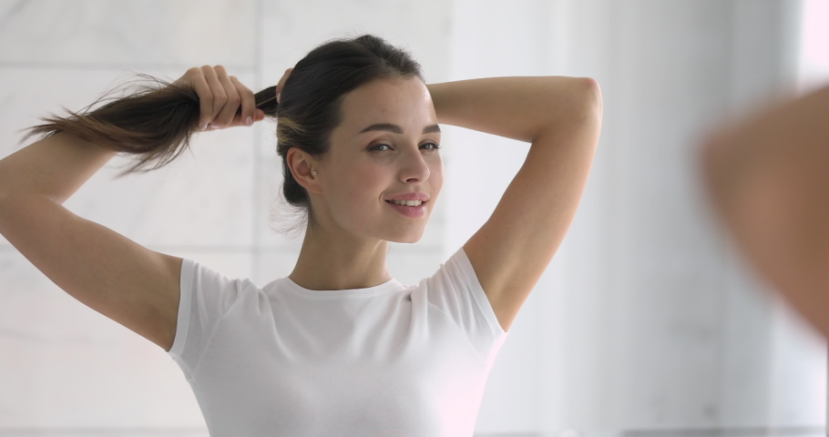 Happy confident young beautiful woman doing long hair style looking in mirror, smiling girl make ponytail hairstyle in bathroom or bedroom in the morning getting ready during everyday routine at home Royalty-Free Stock Footage #1037145023
