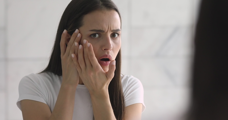 Shocked stressed young woman looking in mirror touching face checking wrinkles, worried depressed girl upset about dark circles frustrated by facial skin problem annoyed by acne pimple in the morning Royalty-Free Stock Footage #1037145035