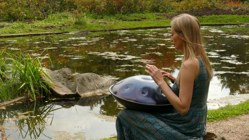 Woman Drummer Playing Music Instrument Hang in park with pond on background