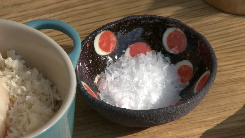 A rough black bowl full of pure white salt on a wooden counter