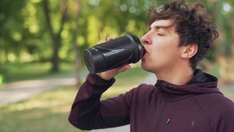 Boy wearing a burgundy hoodie in the park drink from a sport bottle