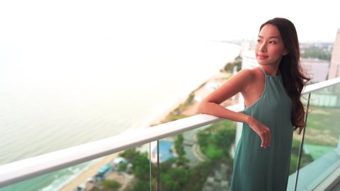 Beautiful Asian woman standing on hotel balcony enjoying sea view. Copy space for text.