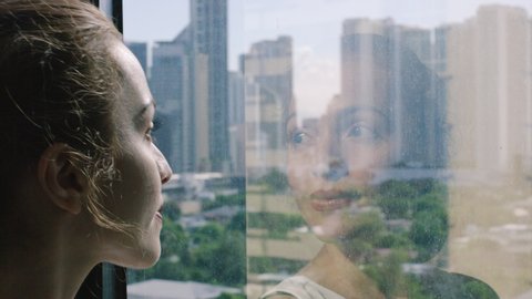 attractive young woman looks in front of a window with the reflection of her face. view of the city and buildings, Manila Philippines