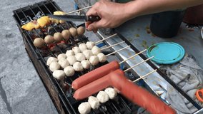 Hand of street vendor's hand is cooking of meatball pork balls and sausage grill on charcoal stove at street food market Thailand. cooking concept. video footage.