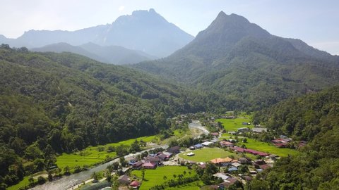 Beautiful aerial drone 4K footage of rural scene in Kampung Tambatuon Kota Belud Sabah with nature river, paddy field, native village and two mountain peak called Mount Kinabalu and Mount Nongkok.