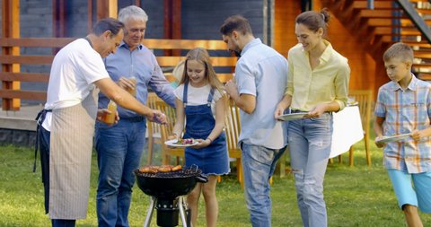 Large multi generation extended family having a barbecue near their house, people enjoying summertime outdoors. 4K UHD