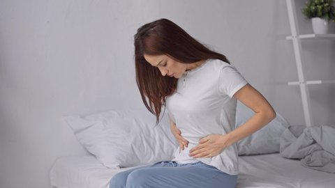 woman sitting on bed in pajamas with stomach ache