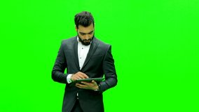 Young man dressed formally using tablet and making hand movements on virtual green screen.